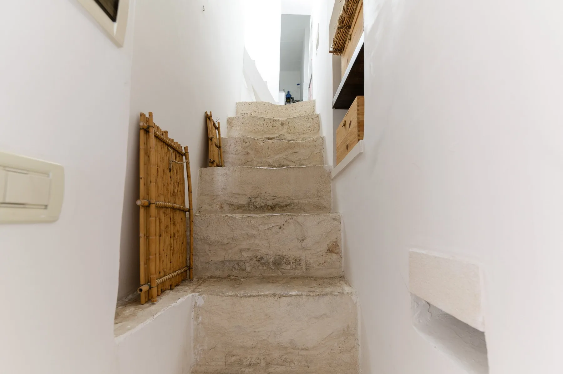 Una escalera interior estrecha con peldaños de piedra clara y paredes blancas.