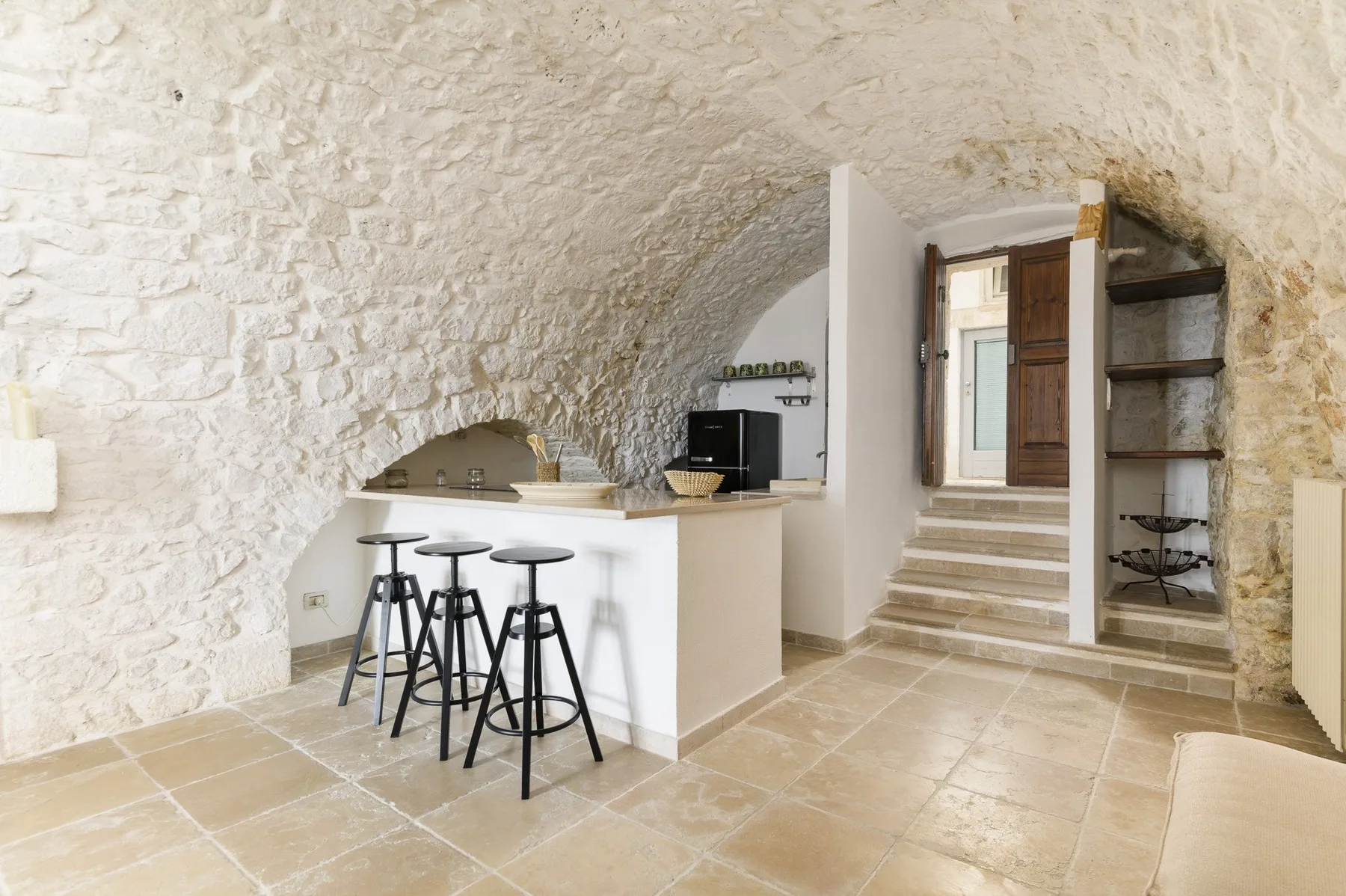 Una cocina de paredes de piedra con una barra y escalones que llevan a una puerta.
