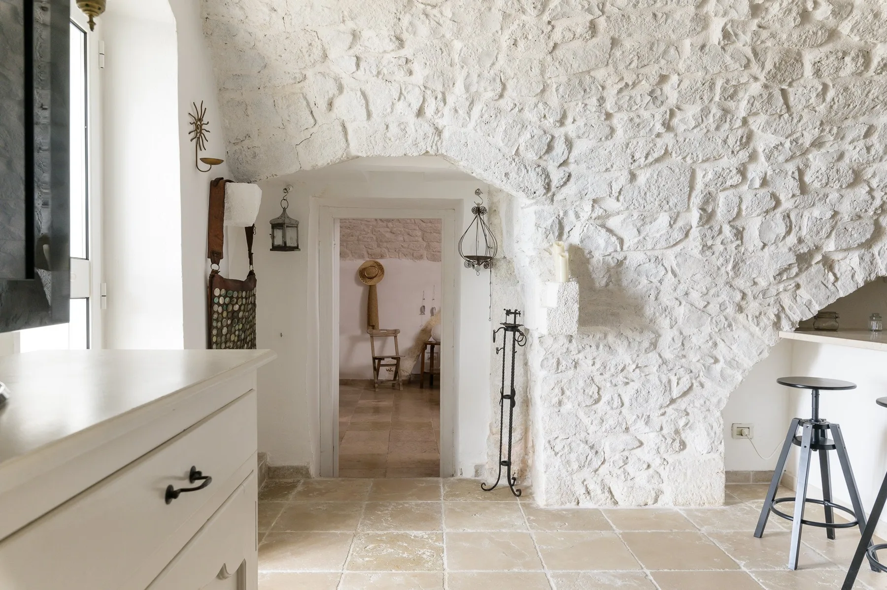 Un interior rústico con una pared de piedra blanca, suelo de baldosas y una puerta.