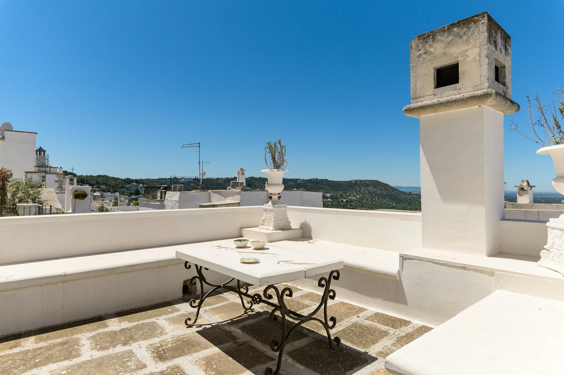 Una terraza soleada en la azotea con una mesa pequeña y muros bajos alrededor.