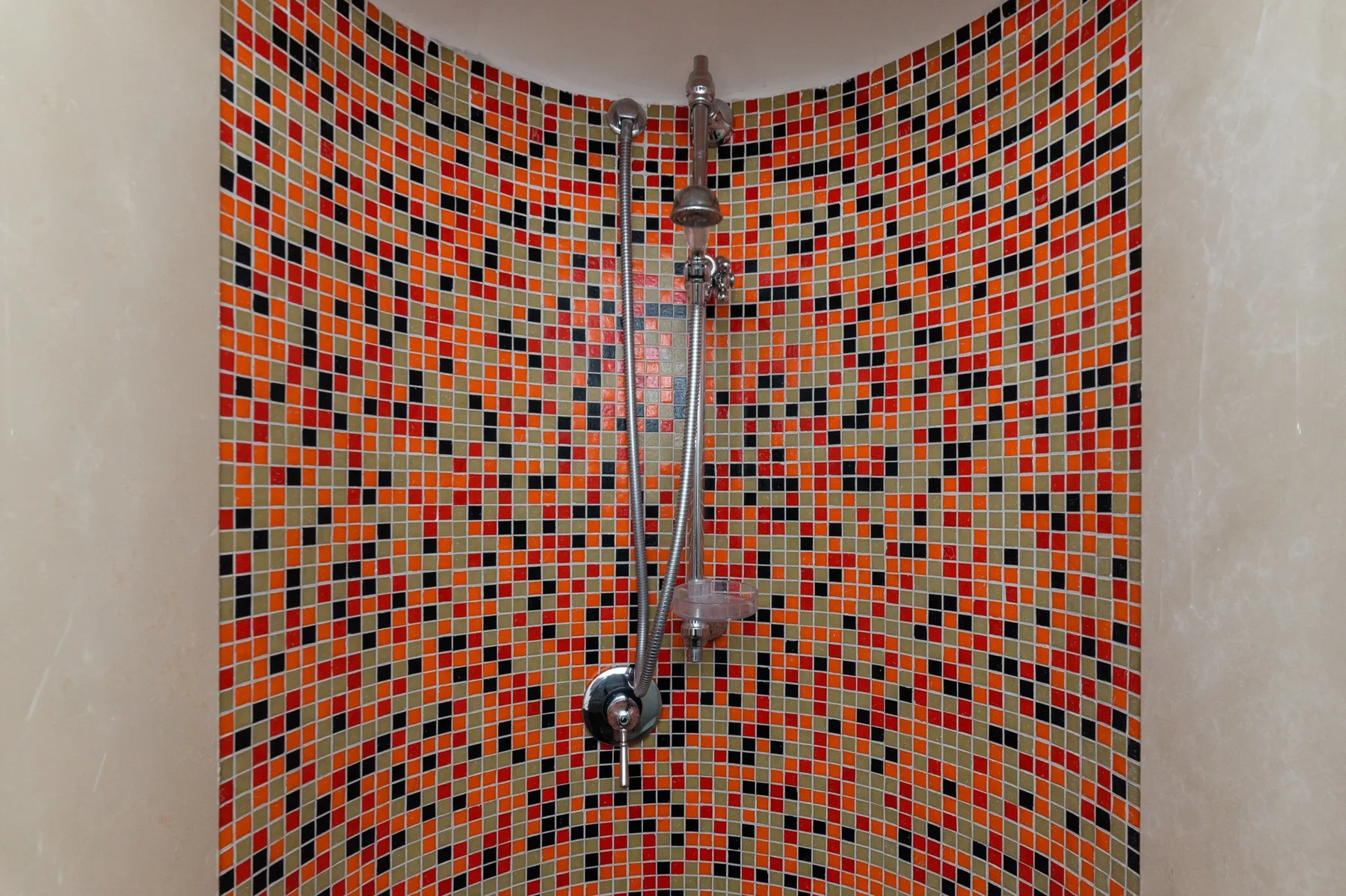 Una ducha con cabezal de mano frente a paredes de mosaico colorido.