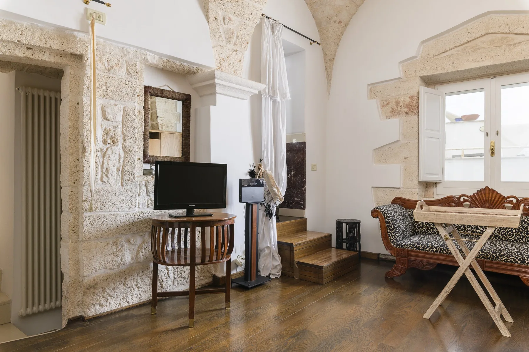 Una sala de estar con paredes de piedra, televisor y asientos junto a una ventana.