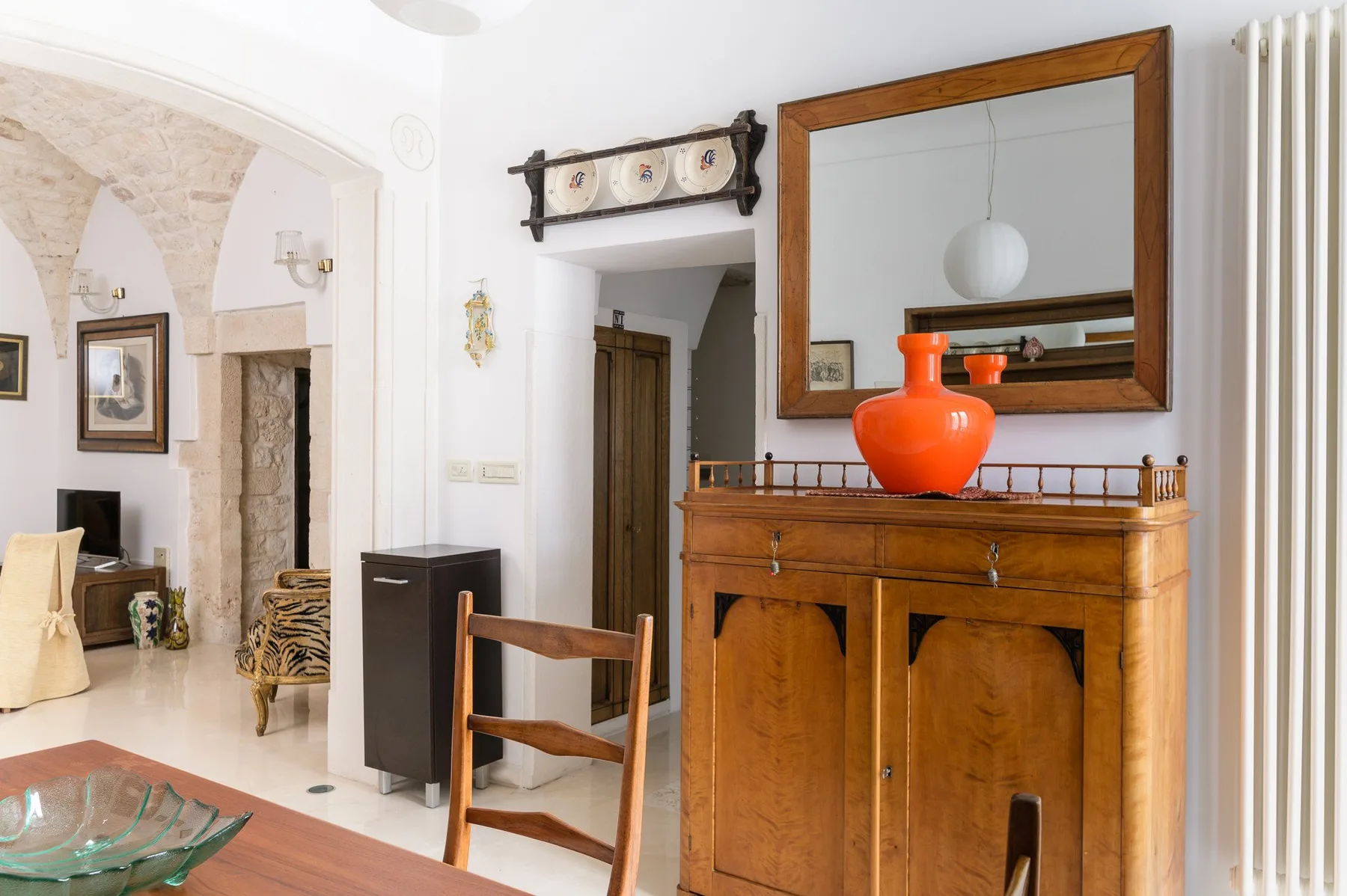 Una sala luminosa con un mueble de madera y un jarrón decorativo rojo.