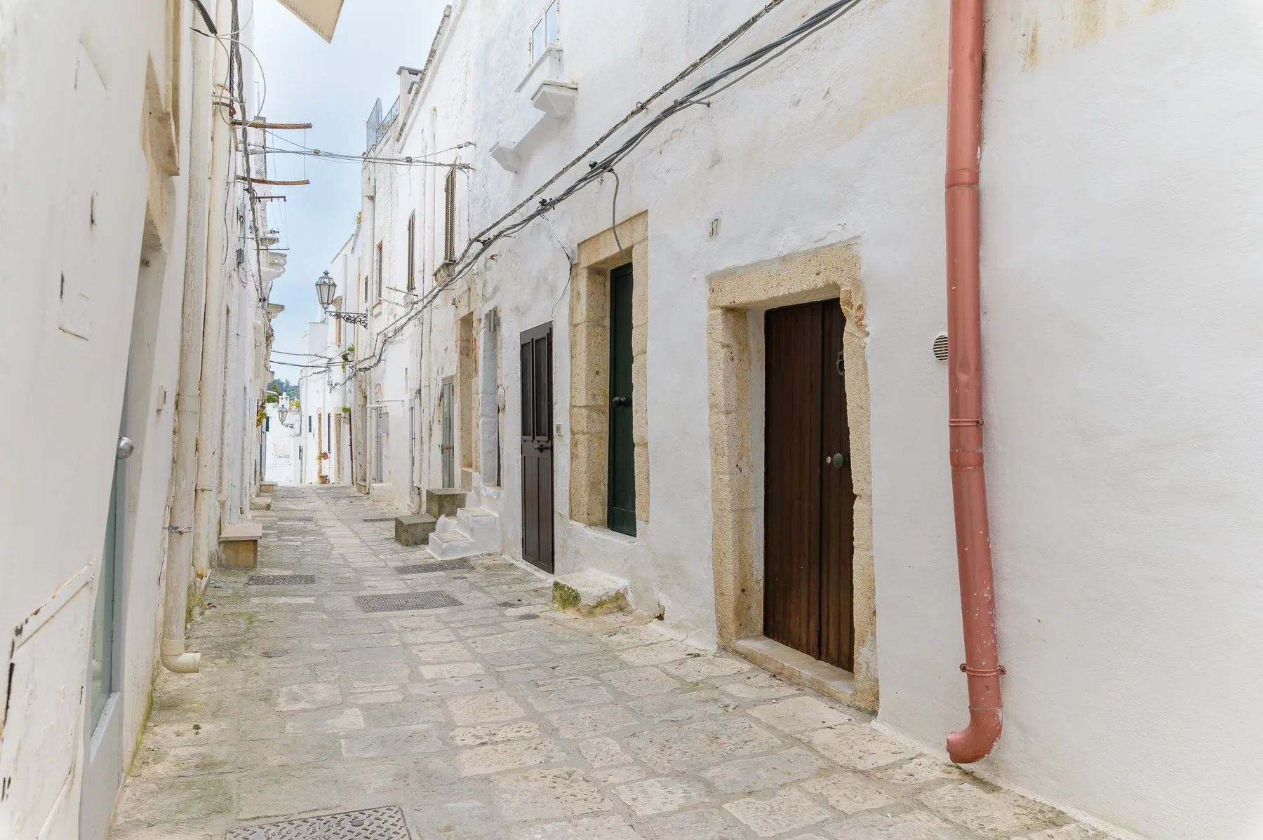 Una calle estrecha empedrada, flanqueada por edificios blancos y puertas oscuras.