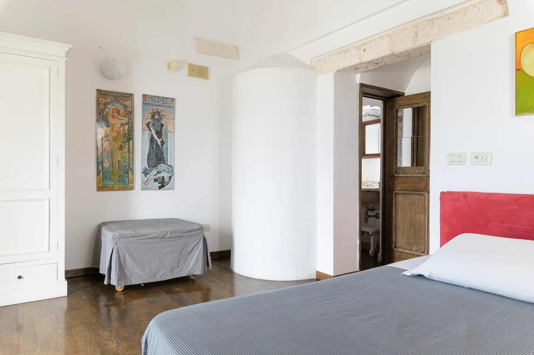 Un dormitorio luminoso con una cama, paredes blancas y una puerta de madera abierta.