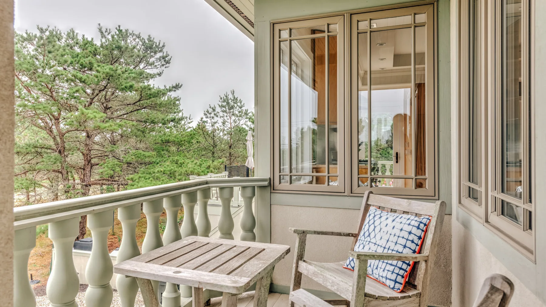 A balcony with a small table and cushioned seating overlooks trees.
