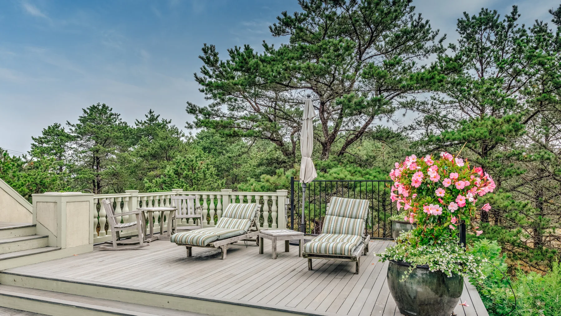 An outdoor deck with lounge seating, a closed umbrella, and potted flowers.