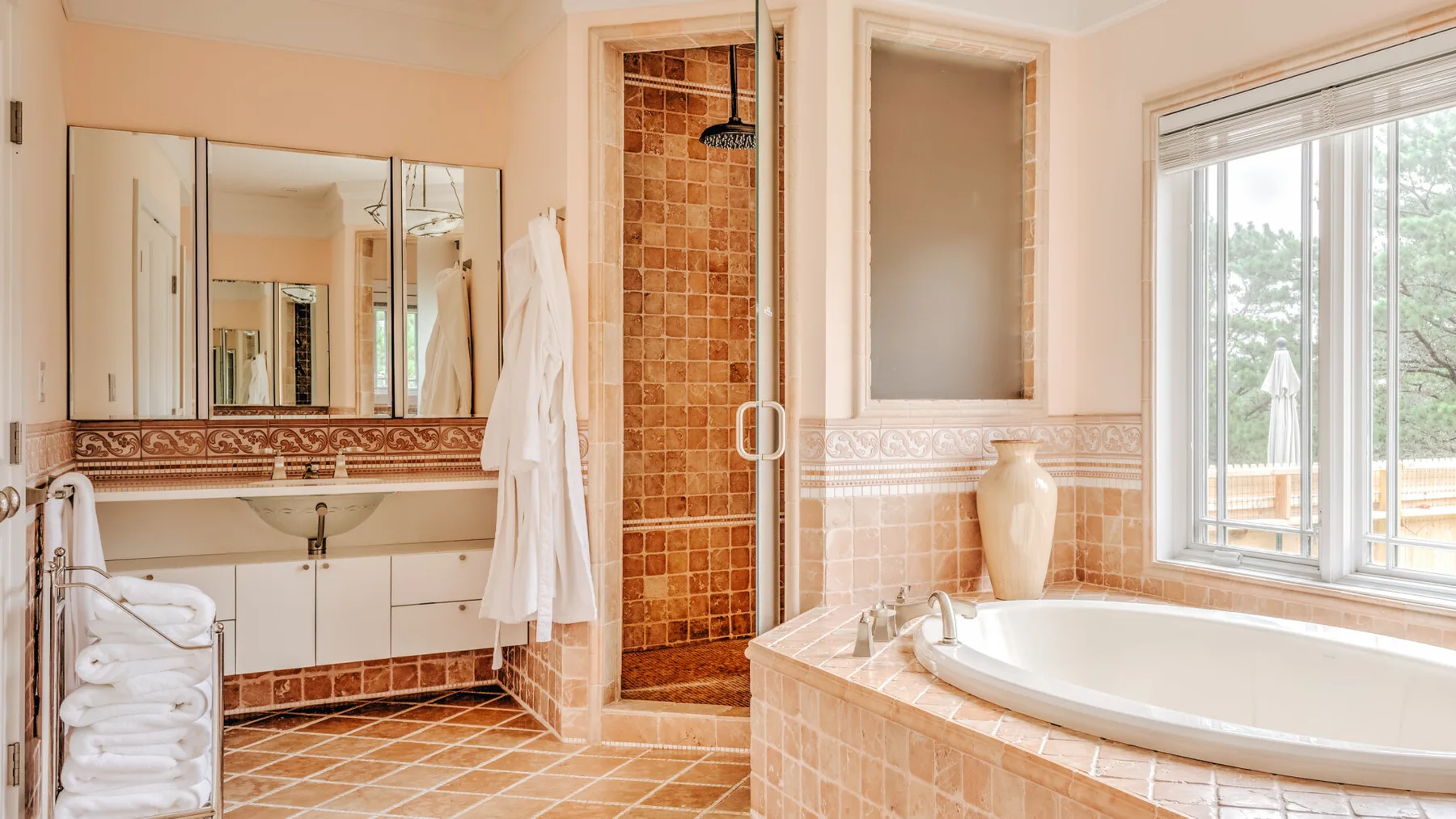 A bright bathroom with a tiled shower, bathtub, and wide windows.