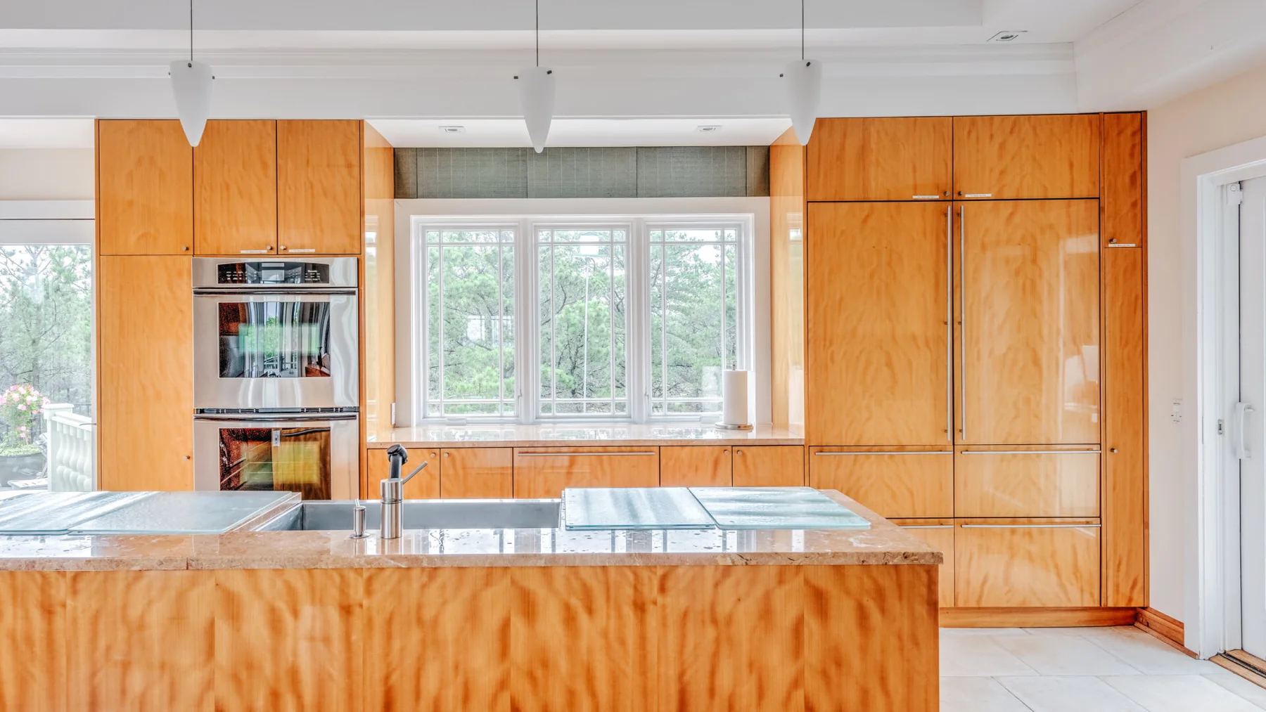 A bright kitchen with wooden cabinetry, a central island, and windows overlooking greenery.