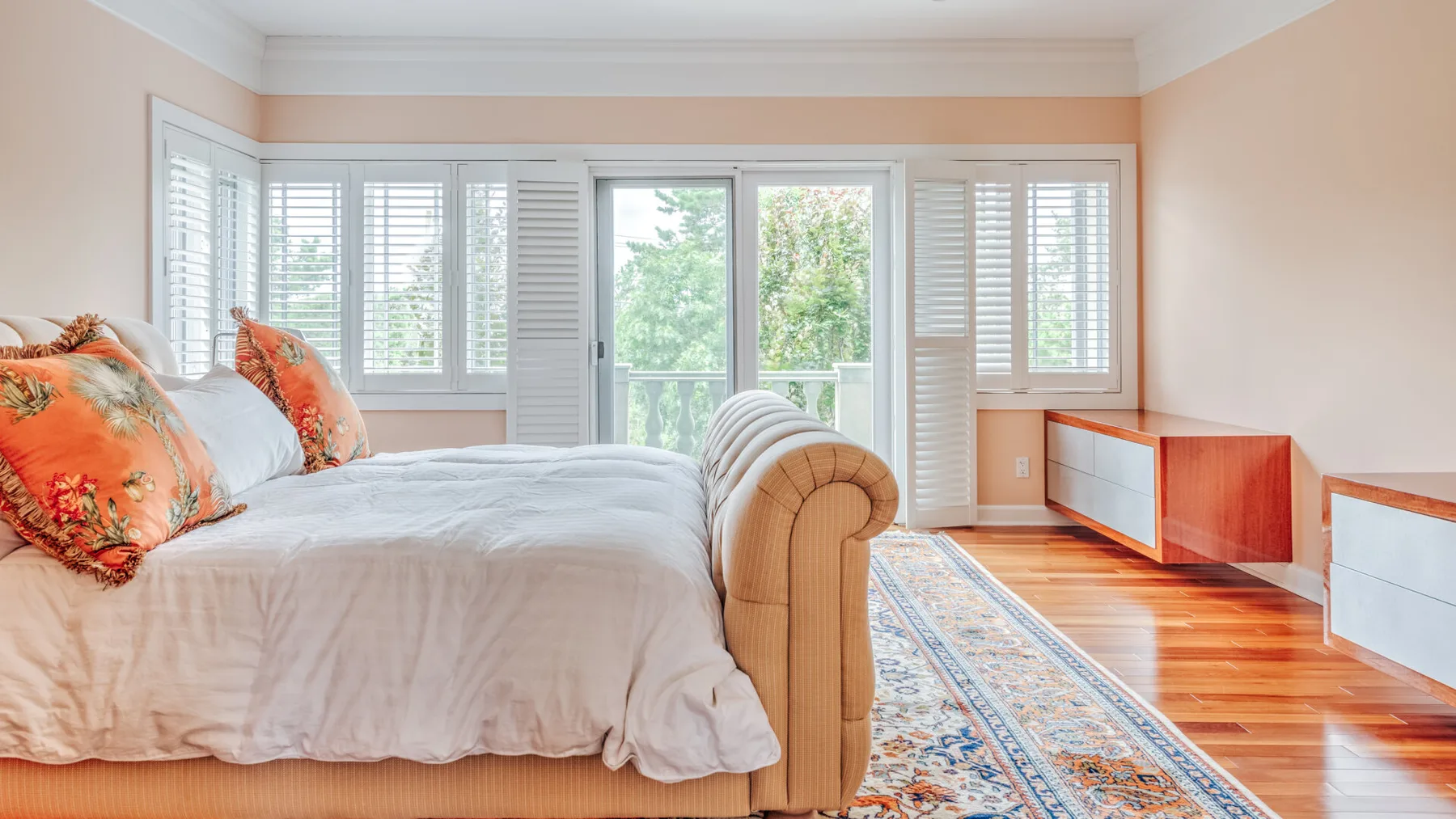 A bright bedroom with a bed, large windows, and a patterned rug.