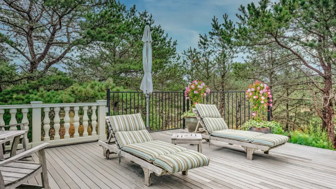 A wooden deck with striped lounge seating and trees surrounding the railing.