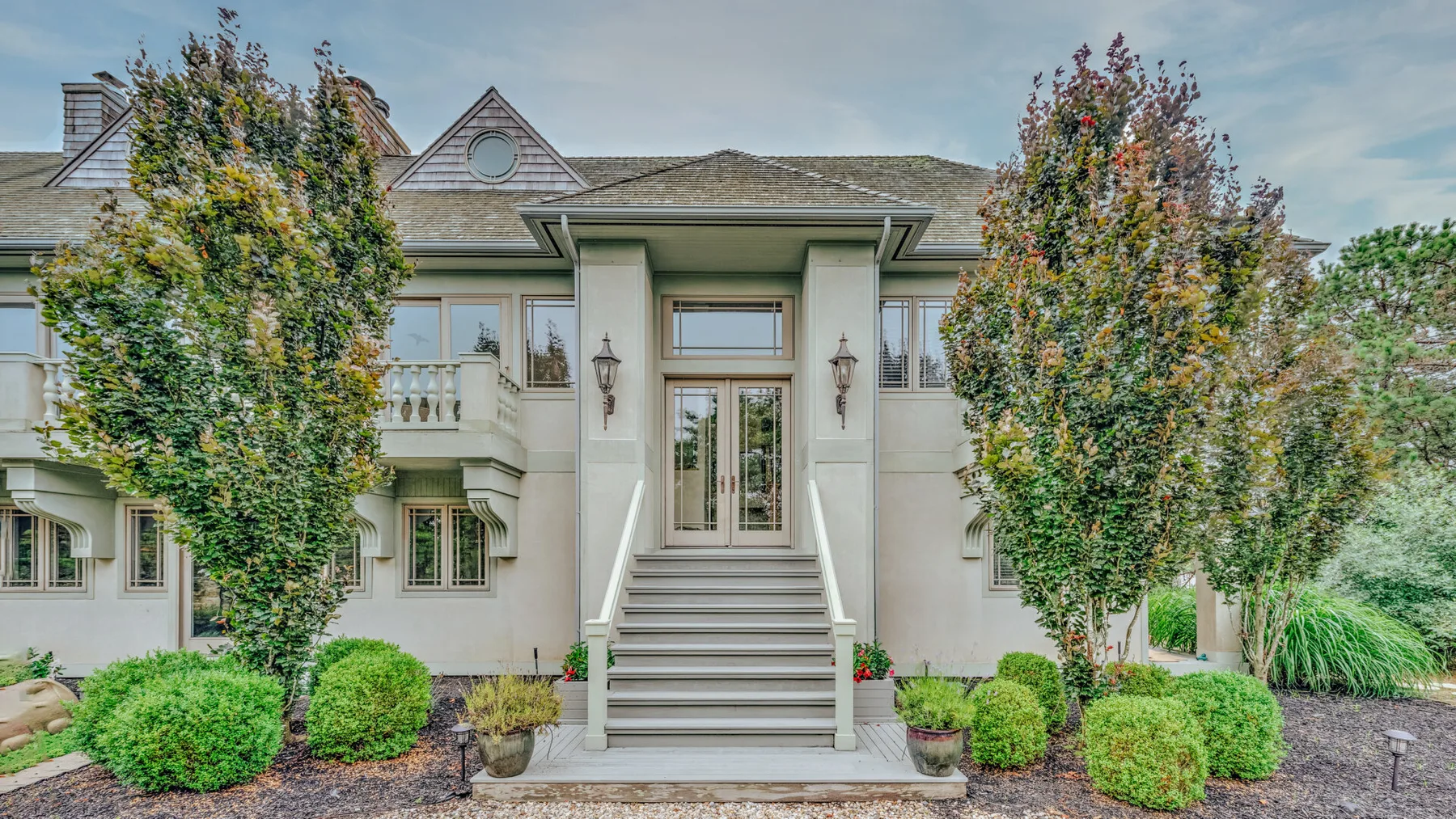 A large house facade has a central entrance with steps and landscaping.