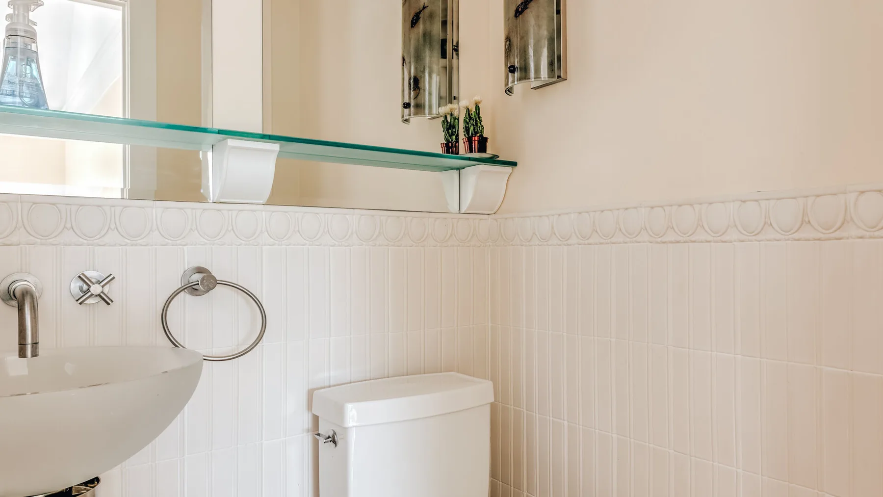 A bathroom with a wall-mounted sink and a toilet beneath a glass shelf.