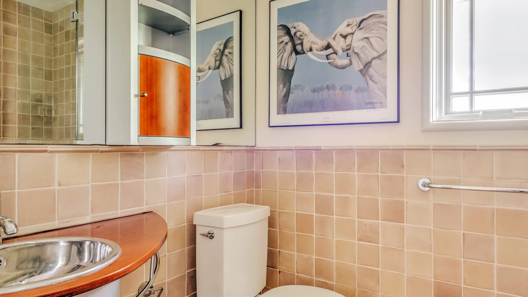 A tiled bathroom with a sink, toilet, and framed elephant pictures.