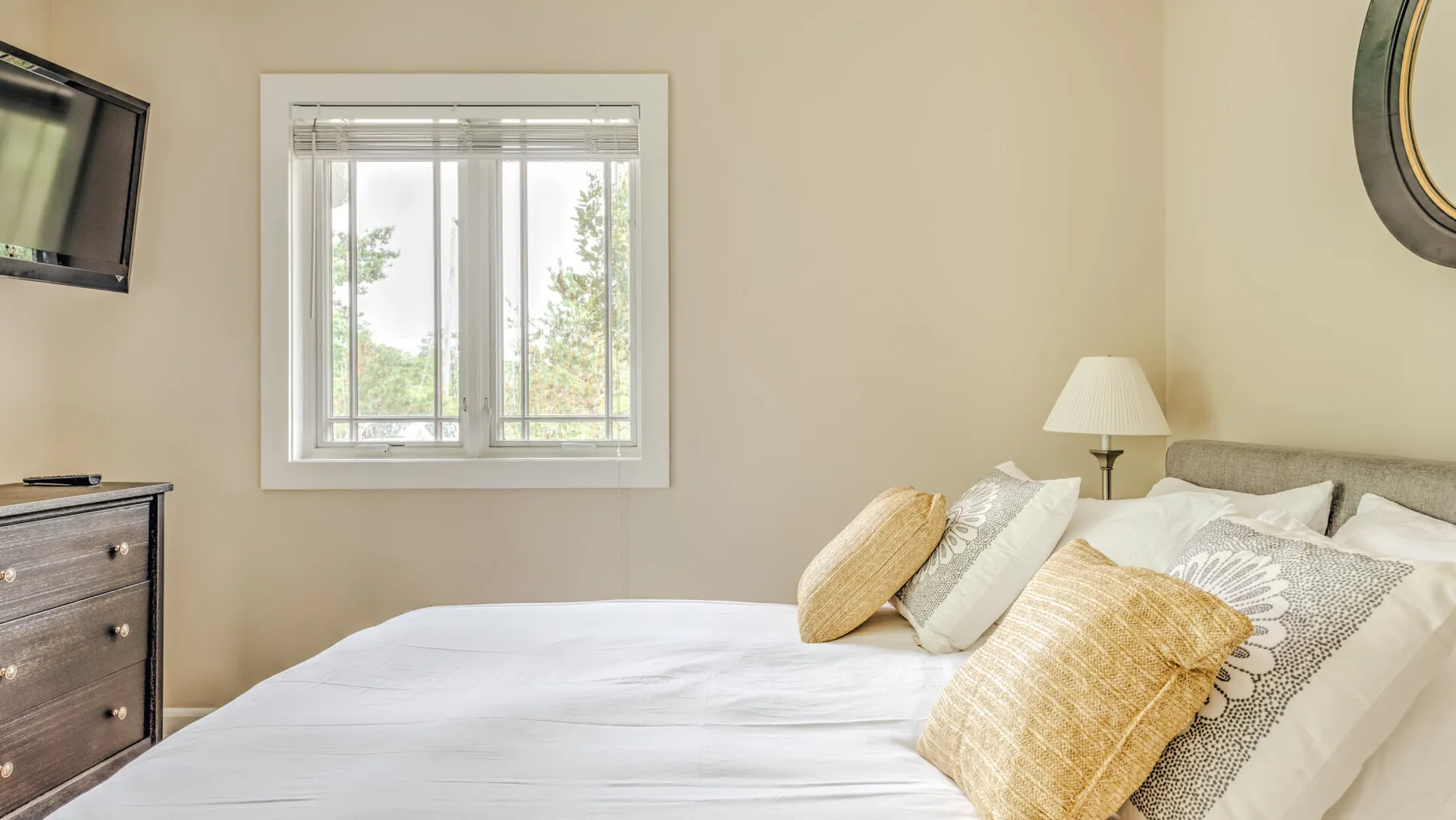 A bedroom with a neatly made bed and a window overlooking trees.