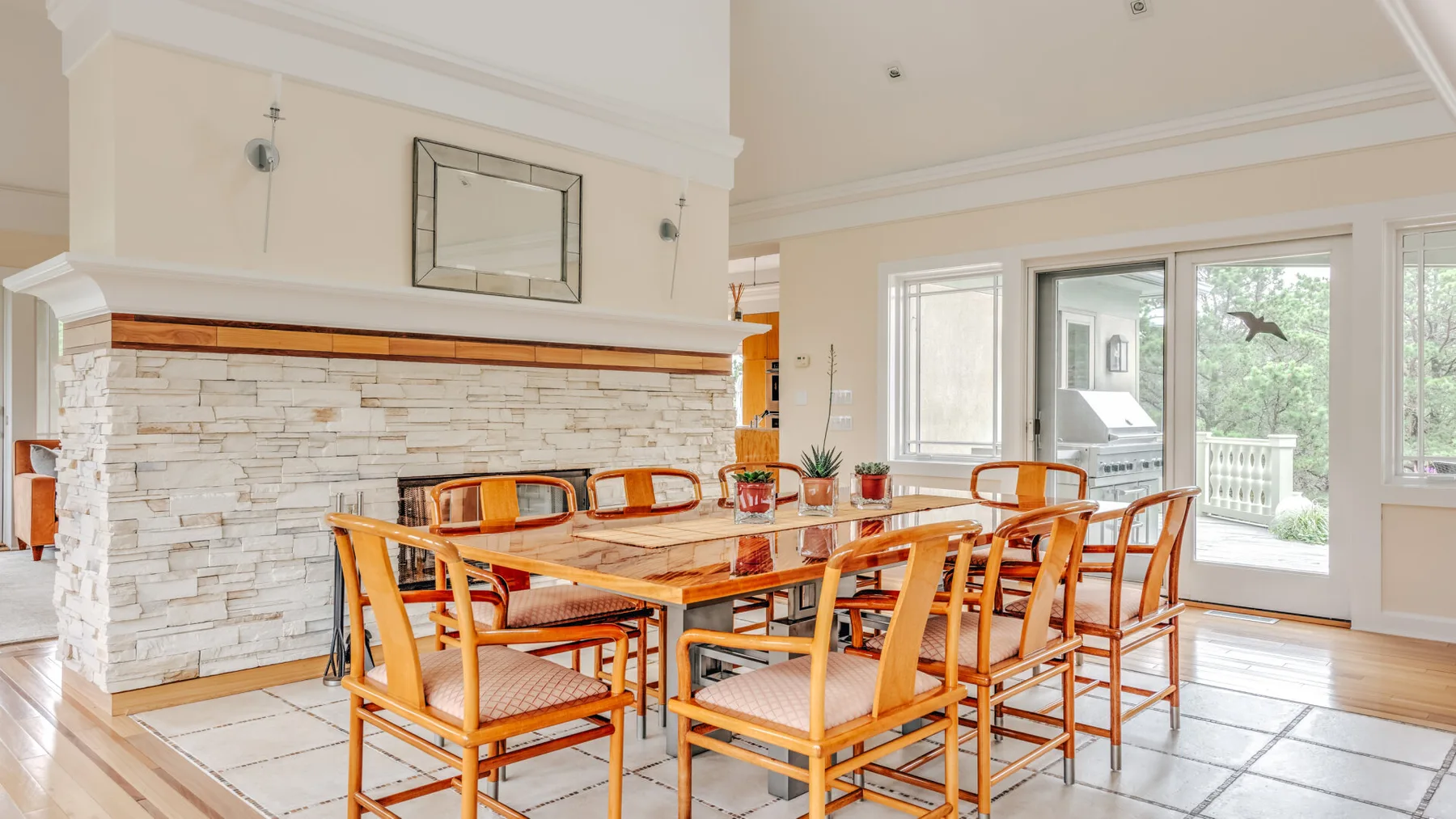 A bright dining room with a wooden table and matching chairs beside large windows.