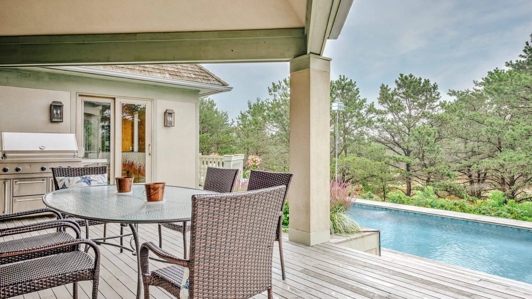 Covered patio with outdoor seating beside a swimming pool and trees.