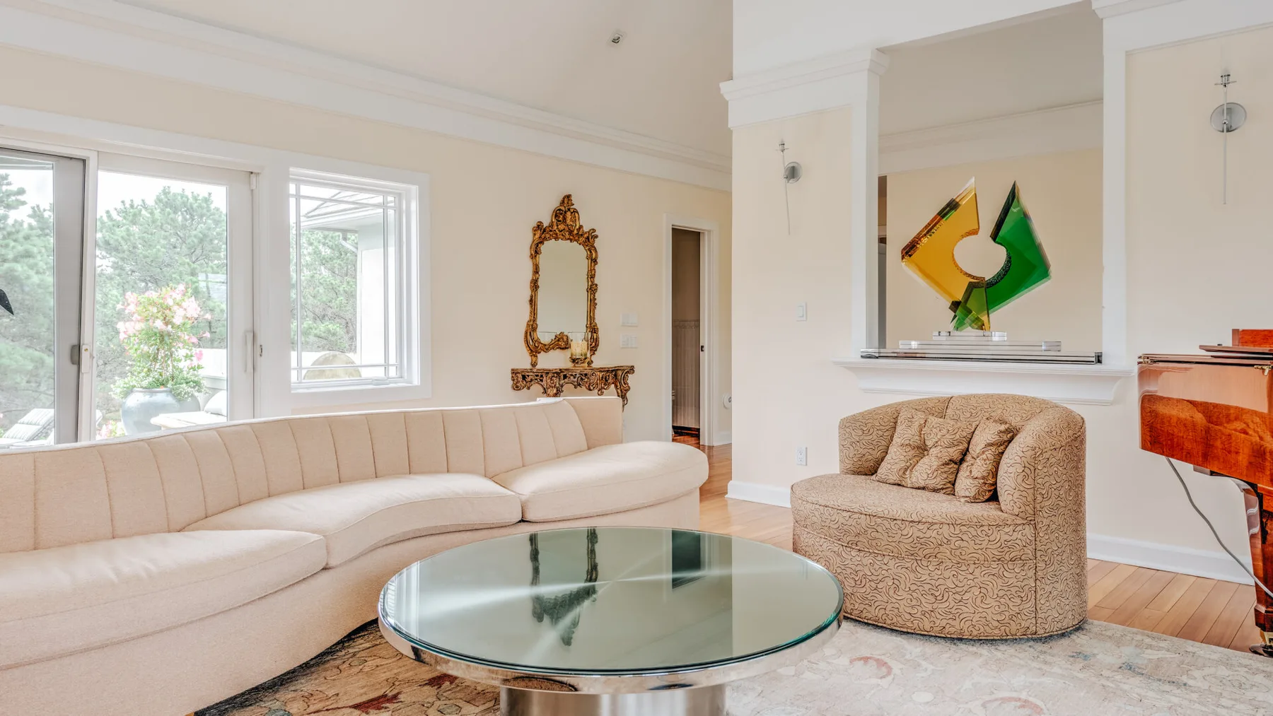 A bright living room with curved seating, a glass coffee table, and large windows.