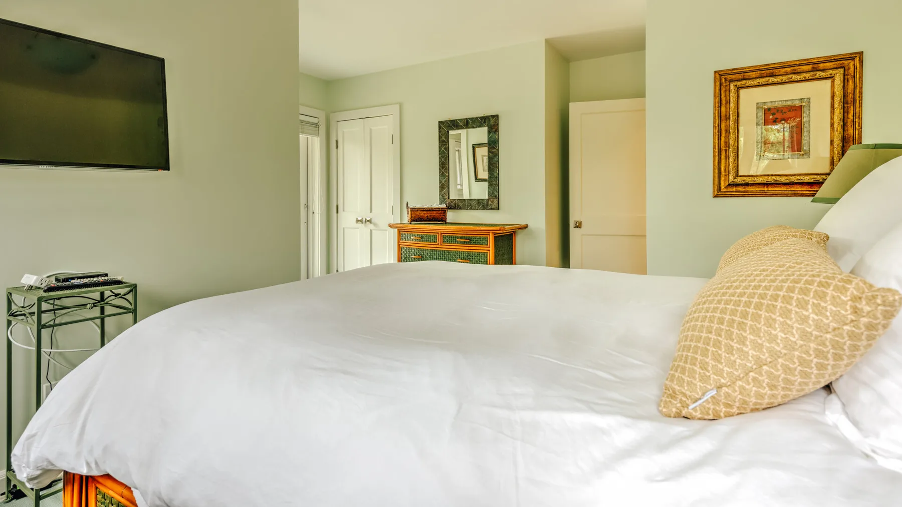 A bedroom with a white bed, bedside table, and framed artwork.