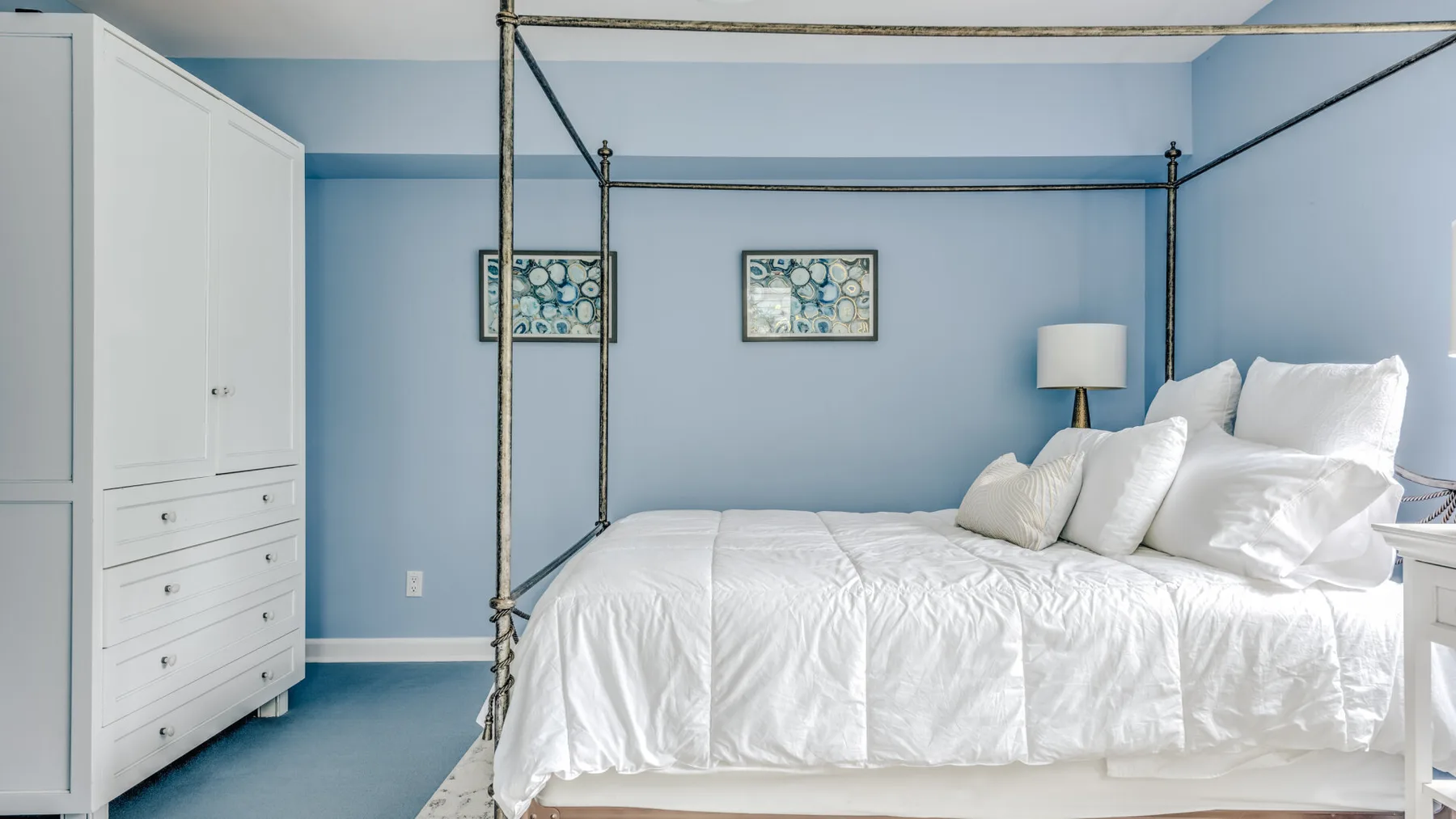A bedroom with a white bed and a tall dresser against light blue walls.