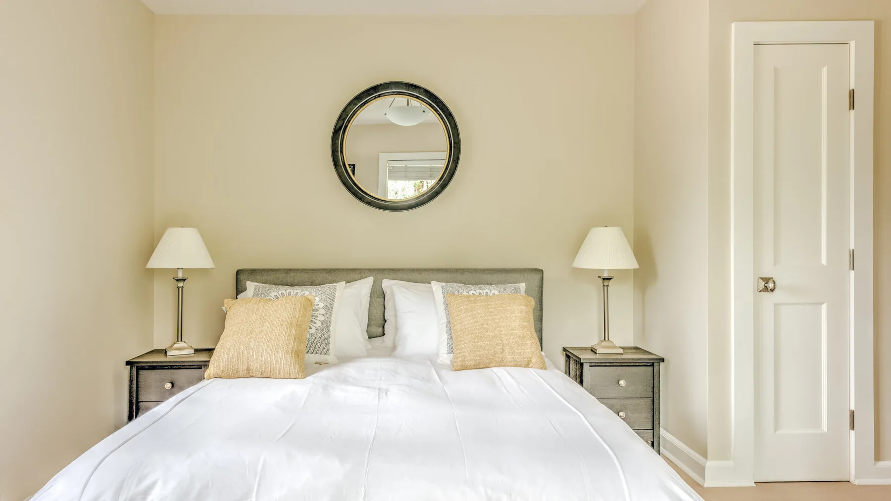 A bedroom with a neatly made bed and a round mirror above the headboard.