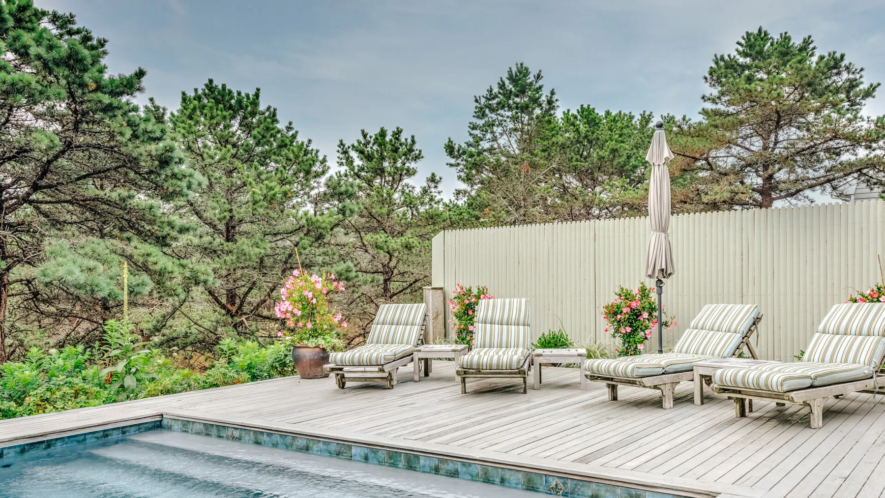 An outdoor deck with lounge seating overlooks a small pool and surrounding trees.