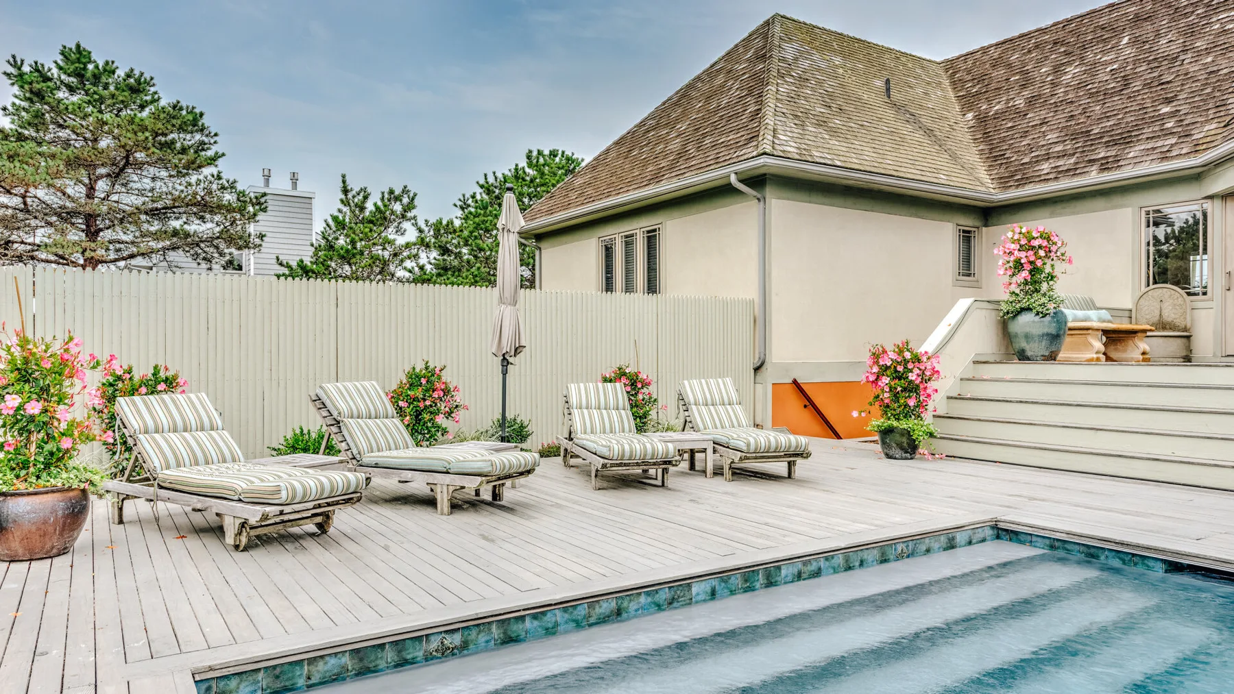 An outdoor pool and deck with lounge seating beside a house.