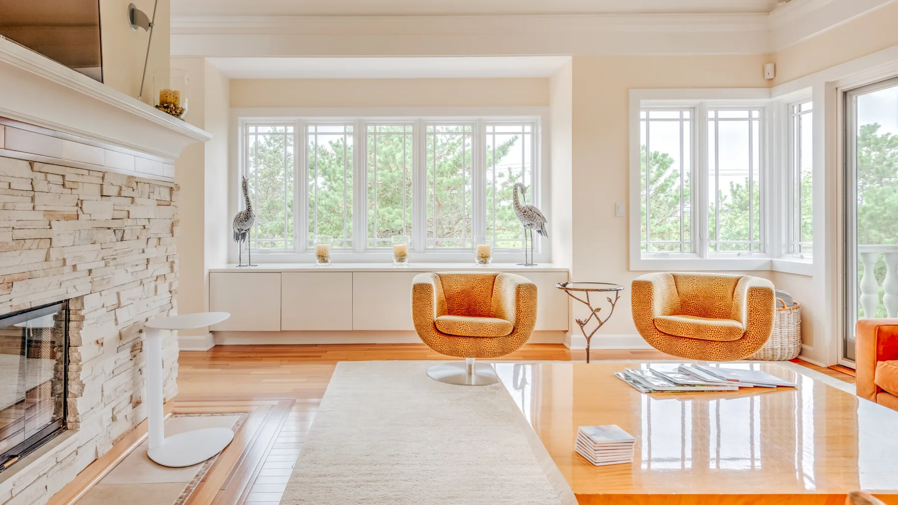 A bright living room with seating arranged beside large windows and a stone fireplace.