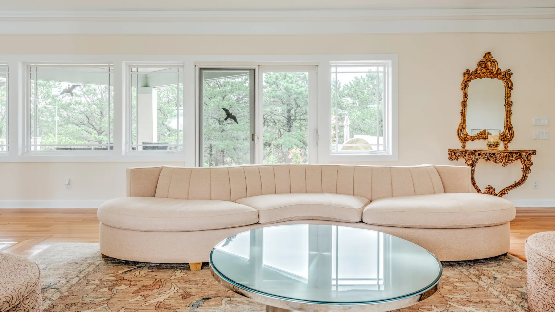 A bright living room with curved seating, a glass coffee table, and large windows.