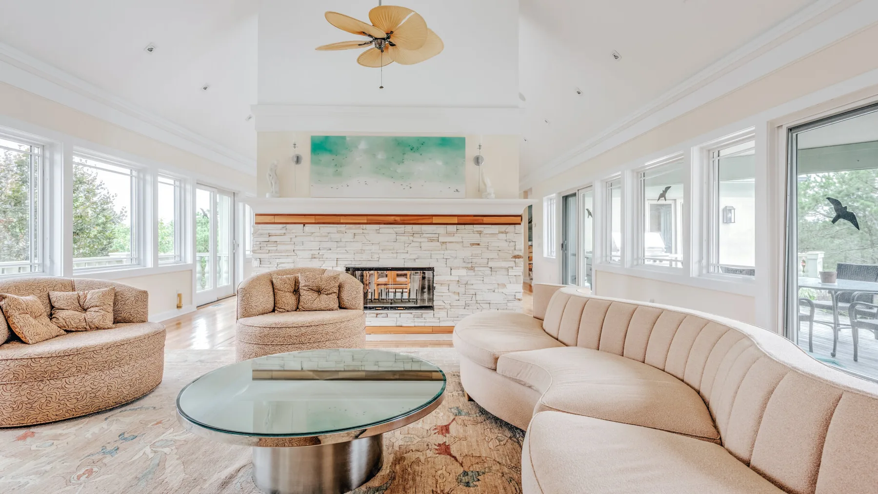 A bright living room with curved seating, a glass coffee table, and a fireplace.