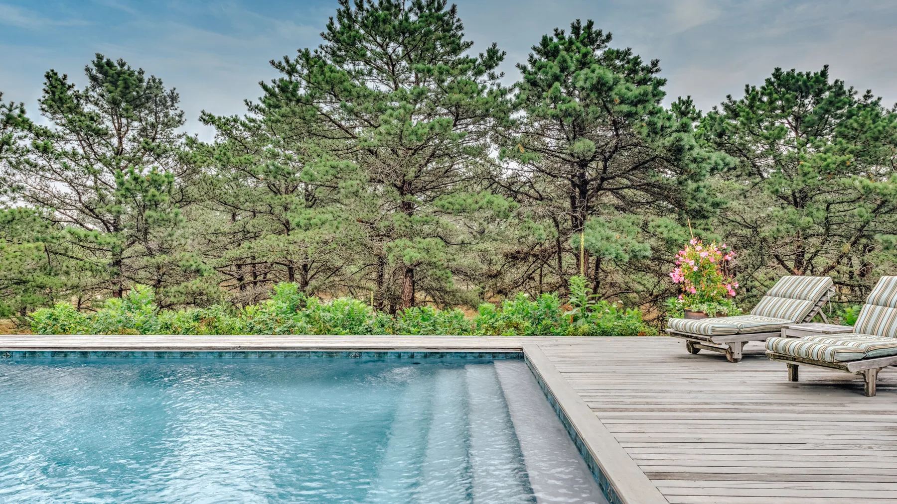 An outdoor swimming pool with a wooden deck and lounge chairs.