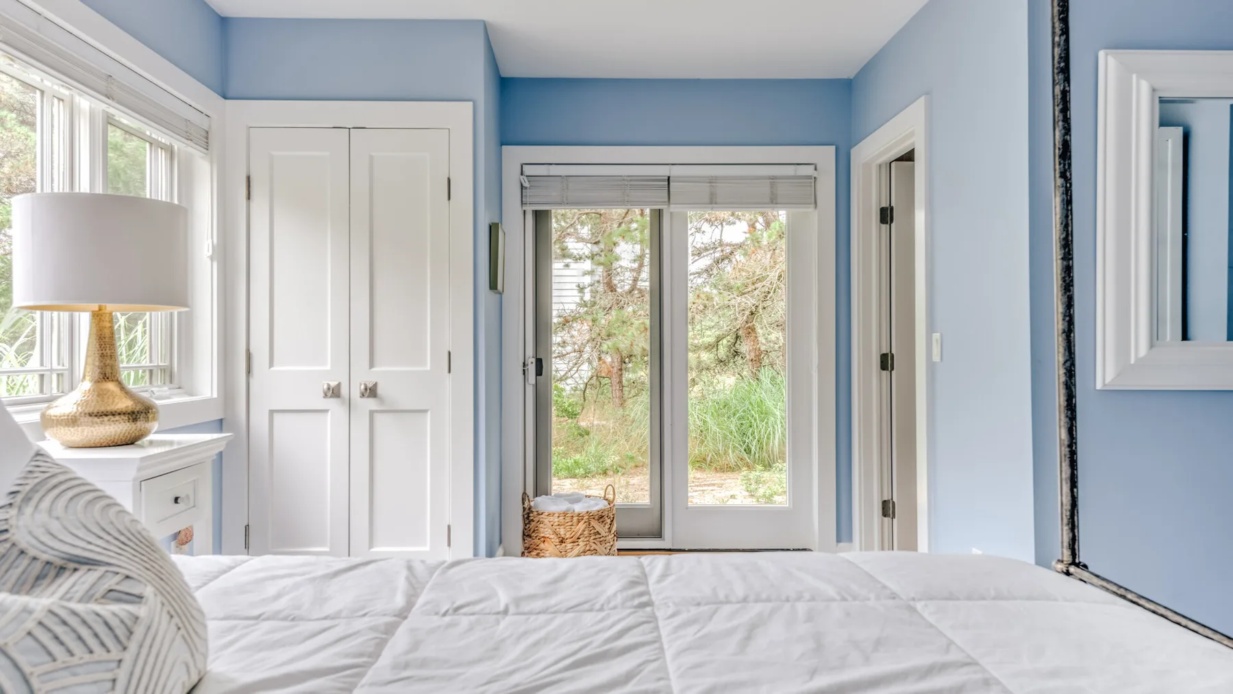 A bright bedroom with a neatly made bed and windows overlooking greenery.