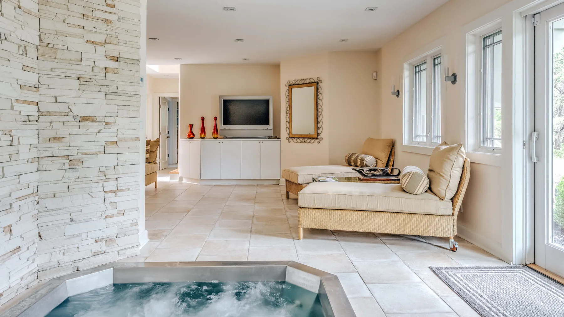A bright living area features a tiled floor, large windows, and a bubbling indoor spa.