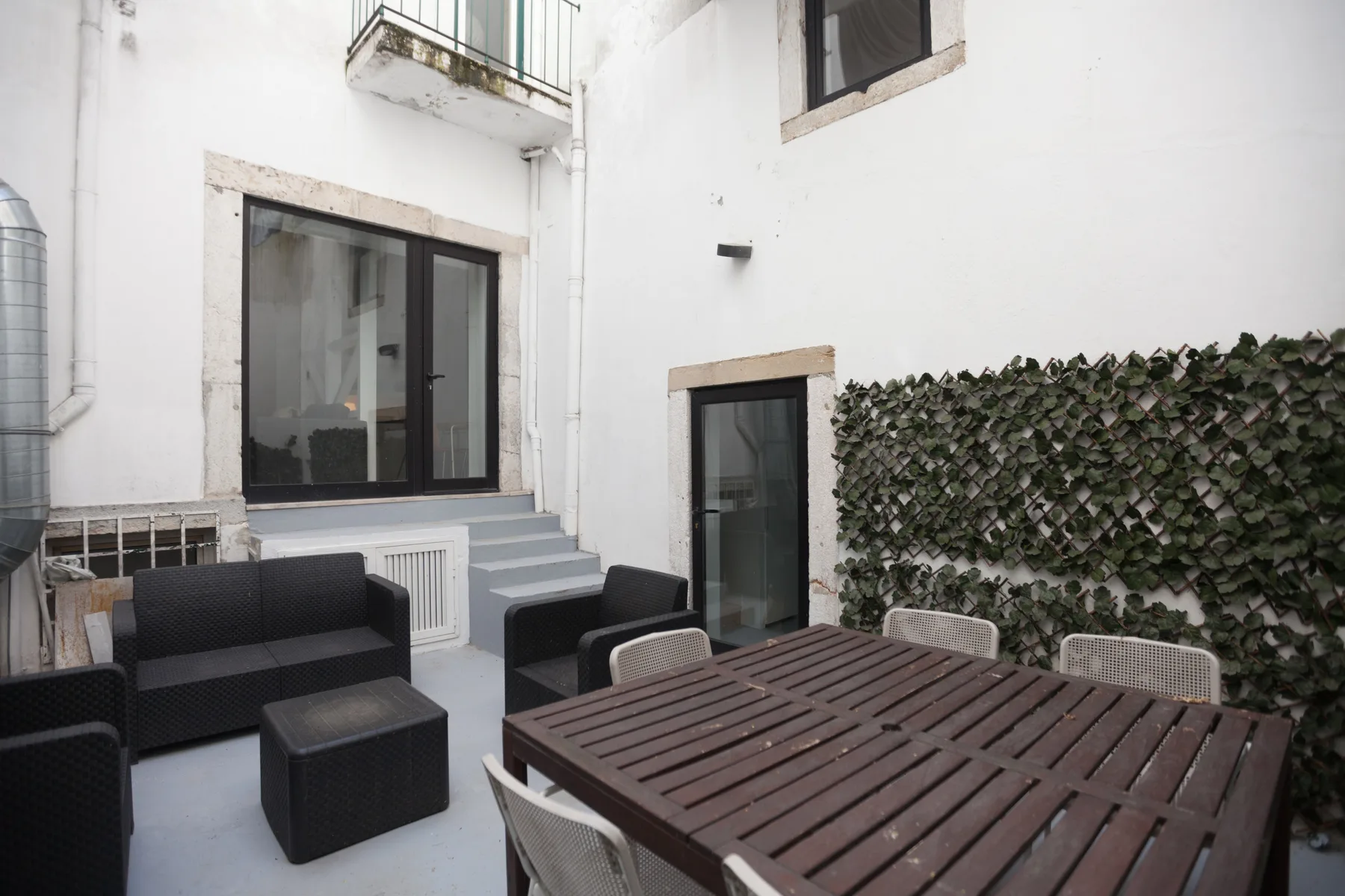 Una zona de comedor exterior con una mesa de madera, asientos y una pared cubierta de plantas.
