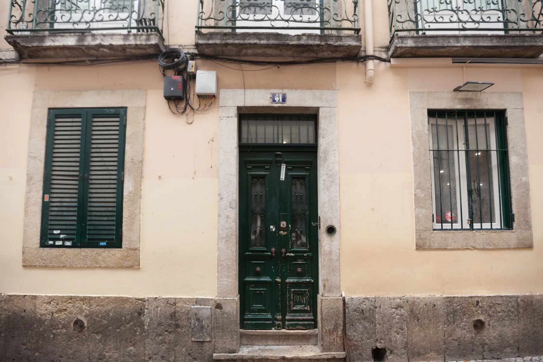 Fachada de un edificio con una puerta de entrada verde oscura y ventanas con contraventanas.