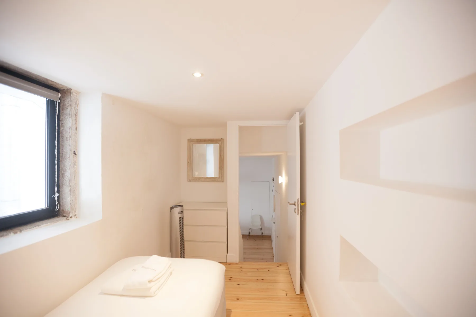 Un dormitorio luminoso con una cama, una ventana y una puerta hacia el baño.