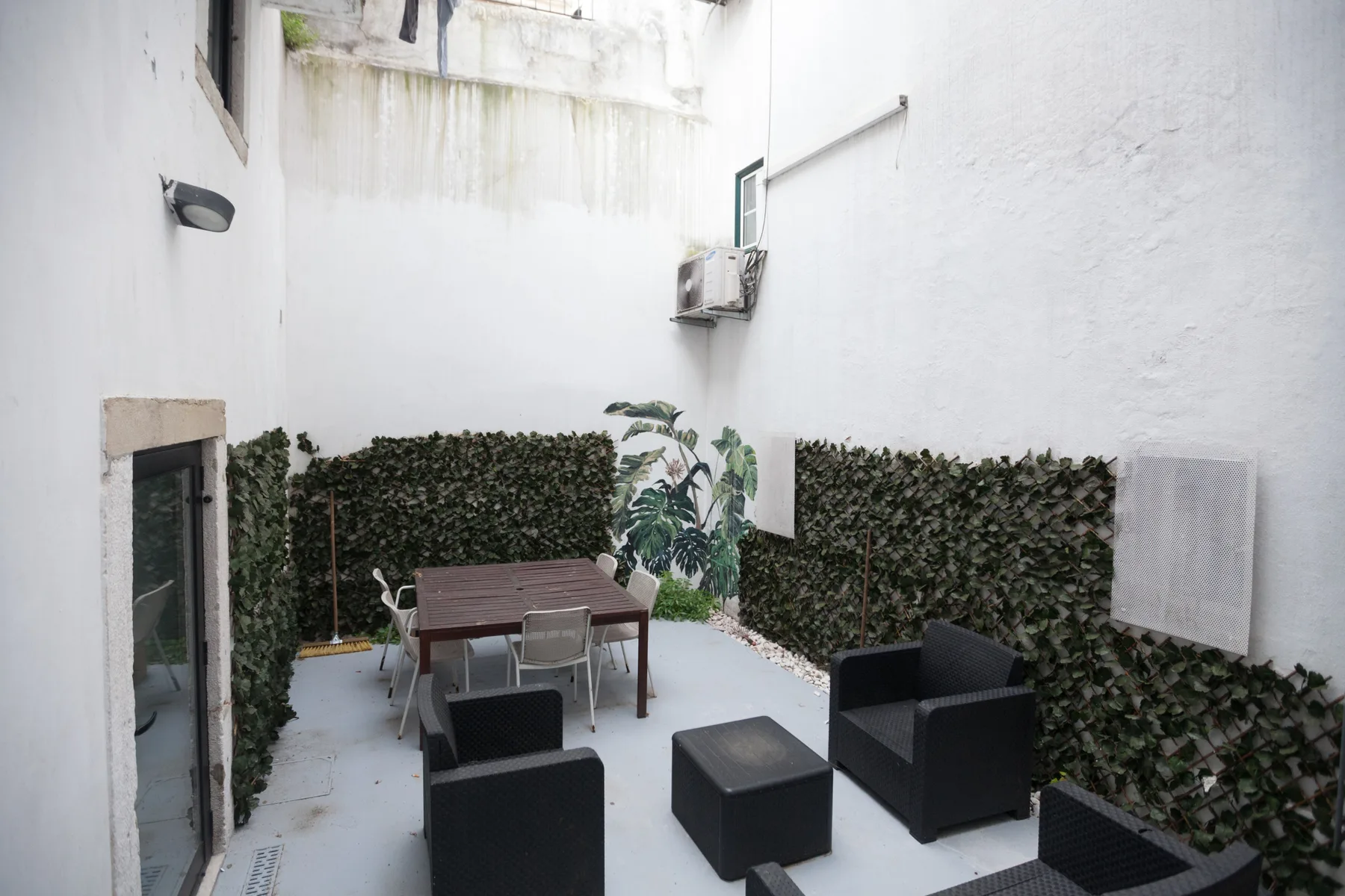 Un pequeño patio exterior con asientos y vegetación frondosa junto a las paredes.