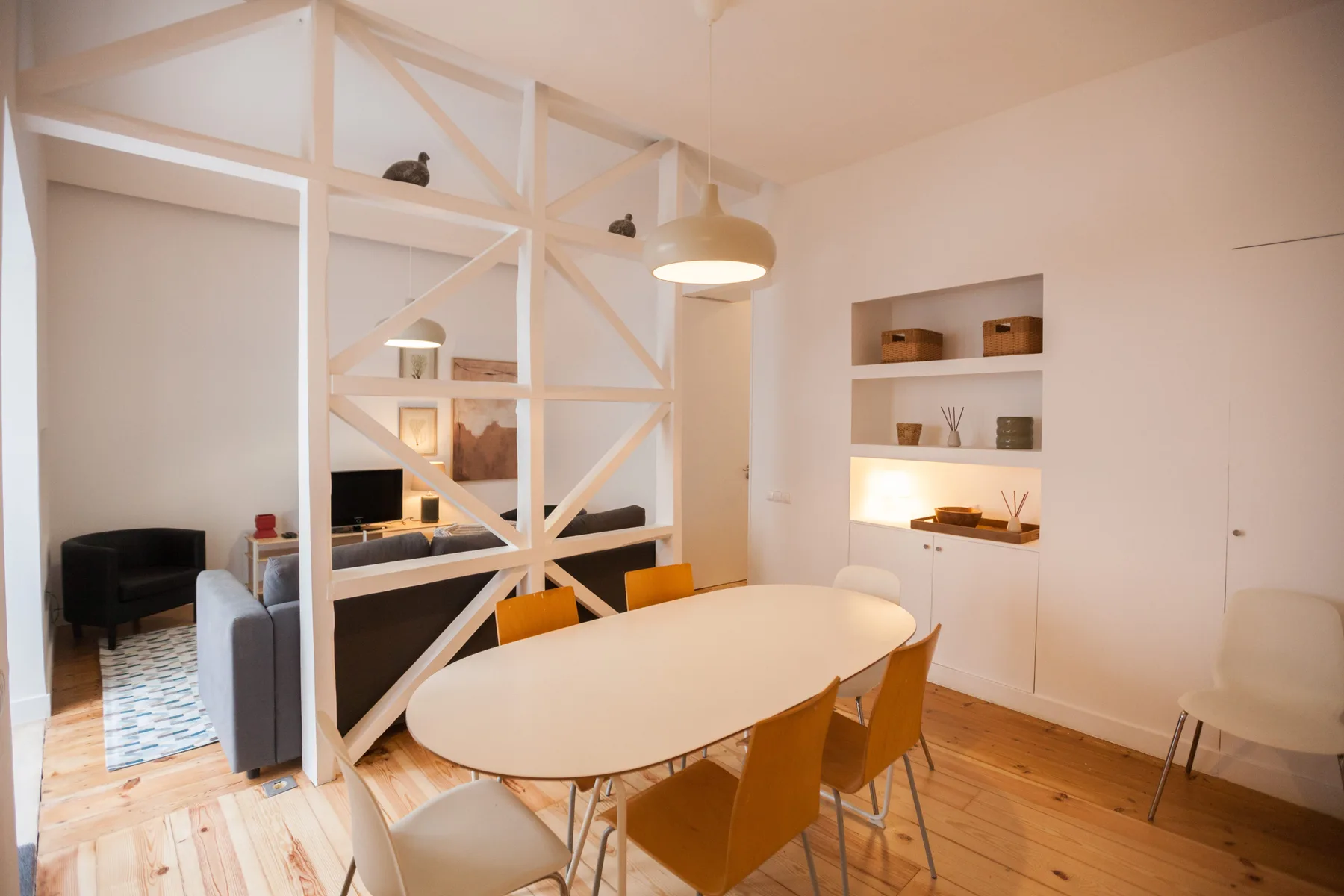 Un comedor con una mesa ovalada junto a una sala de estar separada por una celosía blanca.