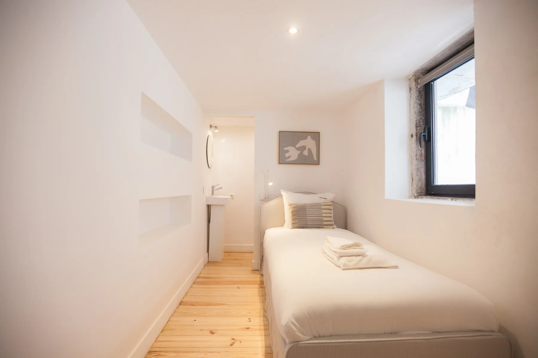 Un dormitorio estrecho con una cama individual junto a una ventana.