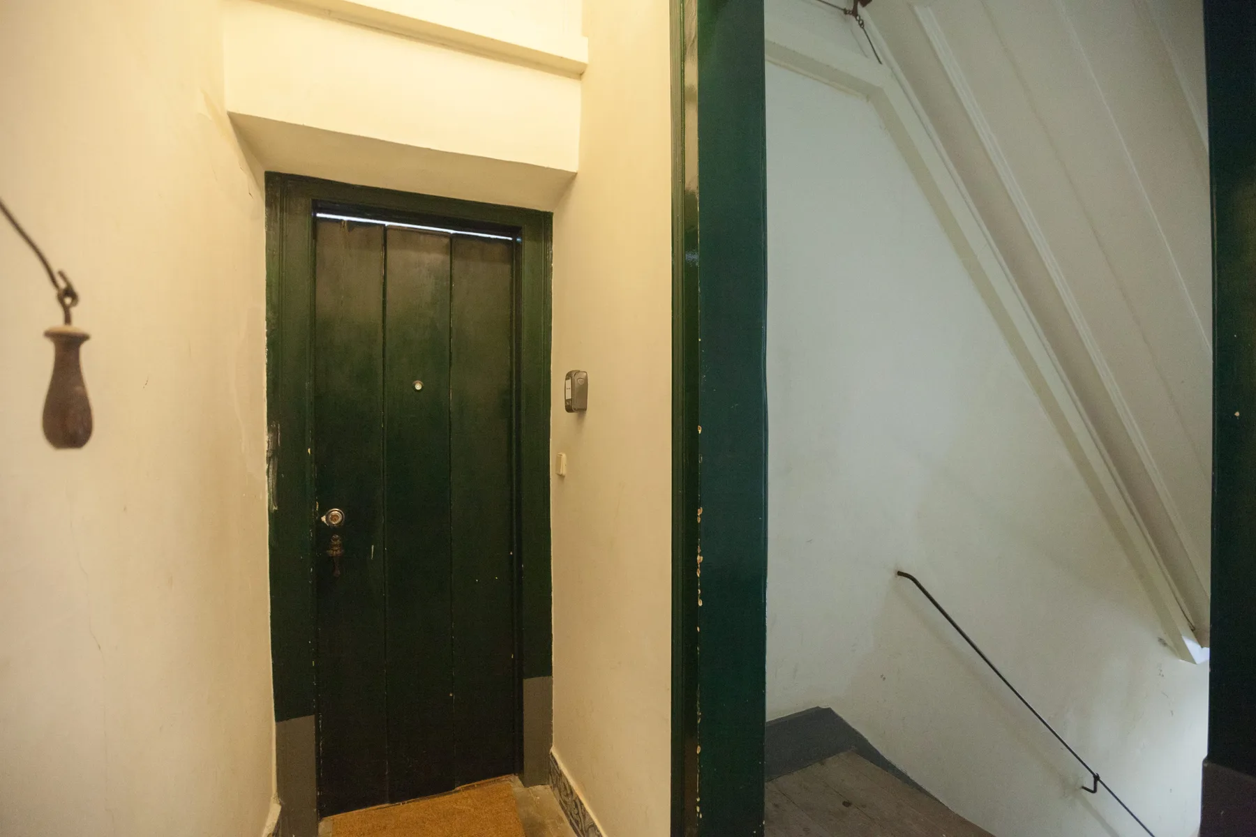 Un recibidor interior con una puerta oscura junto a una escalera.