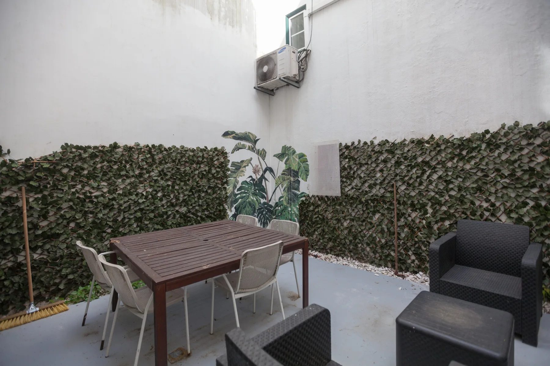 Un pequeño patio exterior con mesa de comedor y asientos junto a muros cubiertos de plantas.
