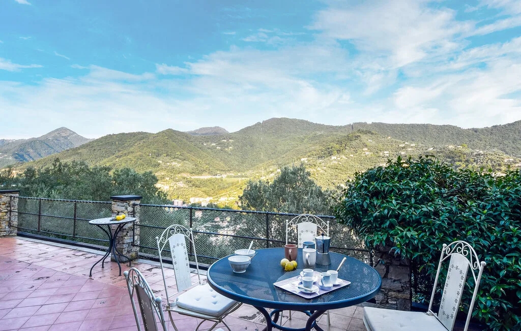 Un patio al aire libre con mesa y asientos ofrece vistas de colinas verdes bajo un cielo azul.