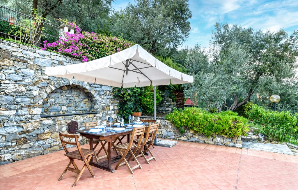 Un comedor al aire libre está bajo una gran sombrilla junto a un muro de piedra.