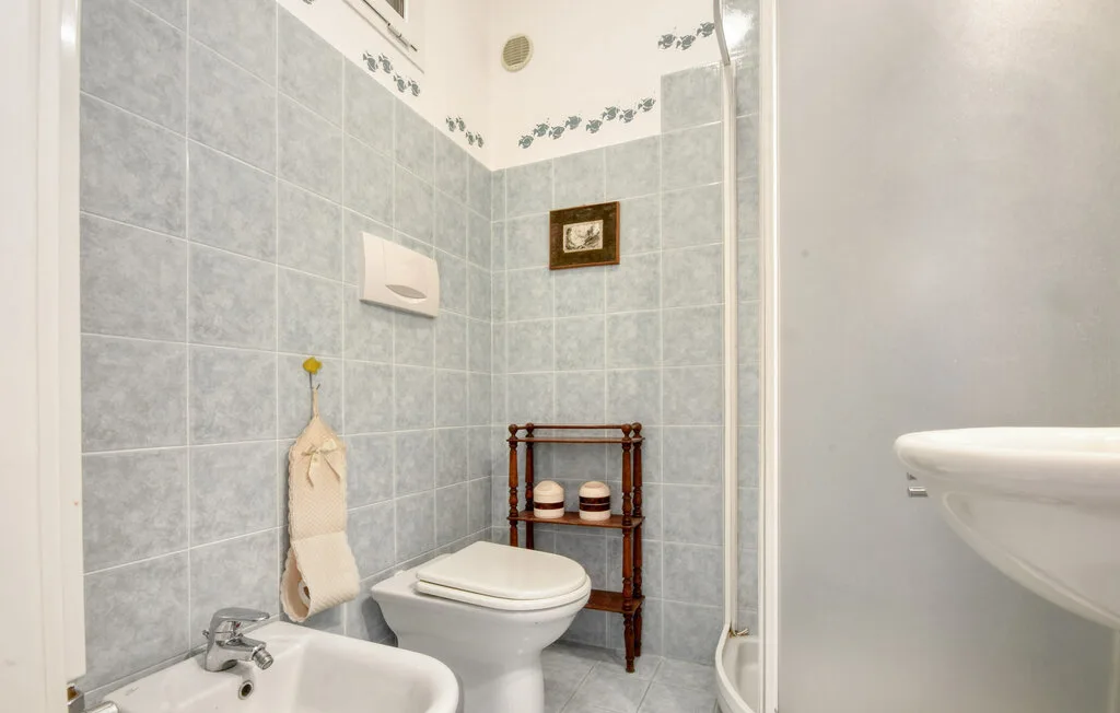 Un baño alicatado con inodoro, lavabo y una pequeña estantería de madera.