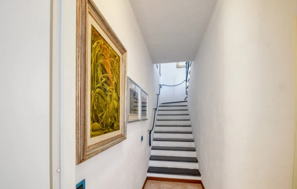 Una escalera interior estrecha sube entre paredes blancas, con cuadros en una pared.