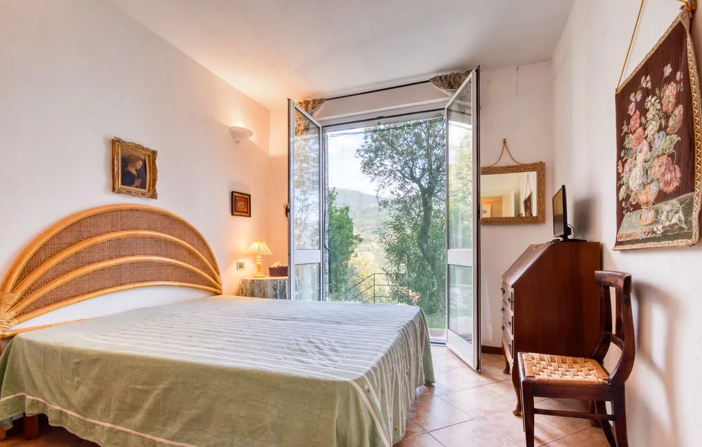 Un dormitorio con una cama junto a una puerta de vidrio abierta y vegetación a la vista.