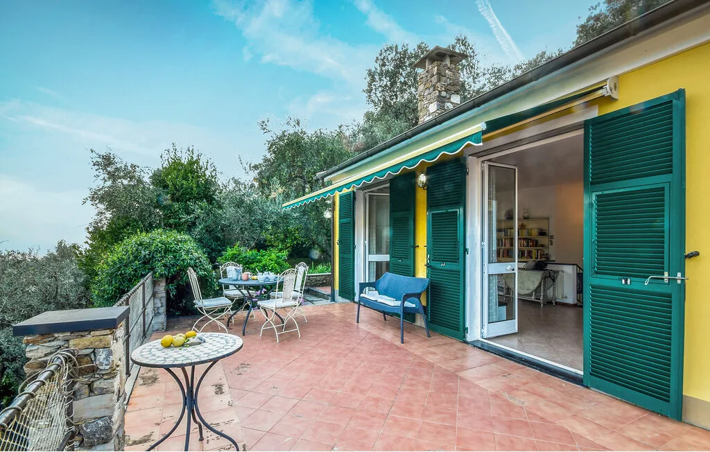 Una terraza exterior con suelo de baldosas, asientos y puertas abiertas a la casa.