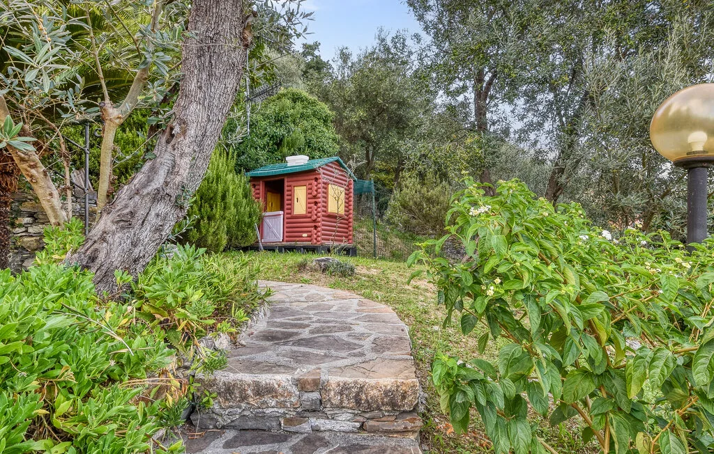 Un sendero de piedra atraviesa la vegetación frondosa y conduce a una pequeña estructura roja de madera.