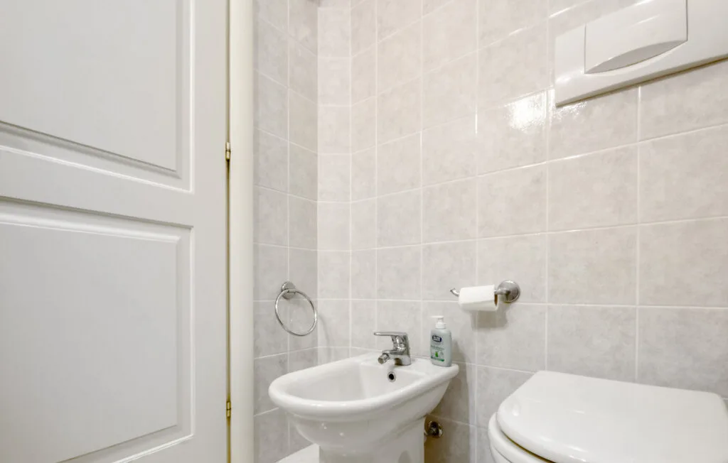 Un baño con azulejos, lavabo e inodoro junto a una puerta blanca con paneles.