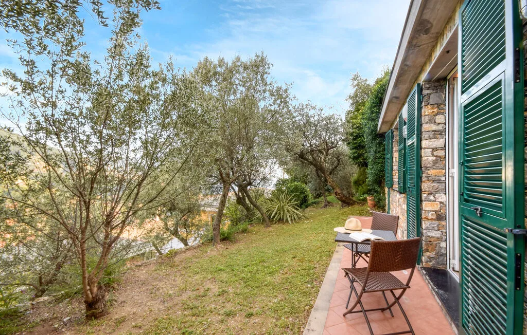 Un patio de jardín junto a una casa de piedra, con asientos al aire libre y árboles.